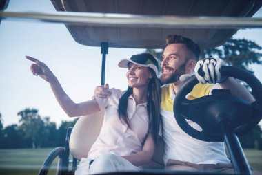 Güzel genç çift konuşmak ve gülümseyen bir golf arabası sürüş sırasında