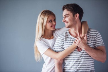 Güzel genç çift sarılma, birbirine bakarak ve gri arka plan üzerinde gülümseyen