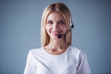 Kulaklık güzel genç kadın kameraya bakarak ve gri arka plan üzerinde gülümseyen