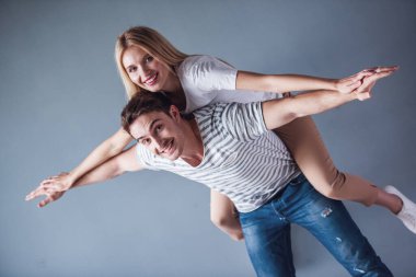 Güzel genç çift eğleniyor, kameraya bakıyor ve gri arka plan üzerinde gülümseyen kız pickaback