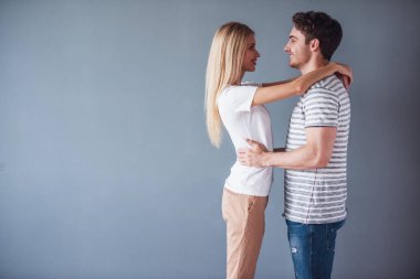 Güzel genç çift sarılma ve gri arka plan üzerinde gülümseyen