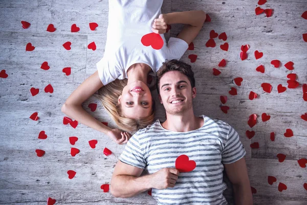 美しい若いカップル赤い紙の心を持って カメラ目線 床に横たわってながら笑顔の平面図 — ストック写真