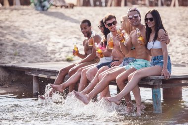 Mutlu arkadaş soda su içme, kameraya bakıyor ve Deniz kenarındaki iskelede otururken gülümseyen