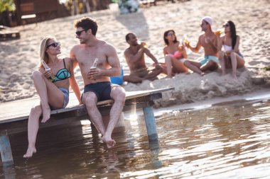 Mutlu arkadaş soda su içme, konuşma ve denizde istirahat ederken gülümseyen