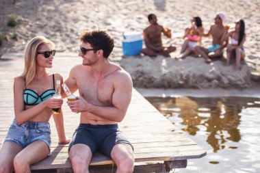 Mutlu bir çift soda su içme, konuşma ve Deniz kenarındaki iskelede otururken gülümseyen
