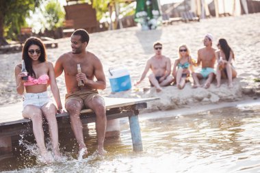 Mutlu bir çift soda su içme, konuşma ve Deniz kenarındaki iskelede otururken gülümseyen
