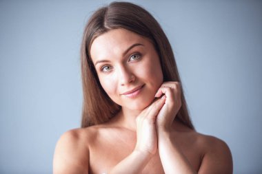 Güzel kadın çıplak omuz ile kameraya bakarak ve, gri arka plan üzerinde gülümseyen