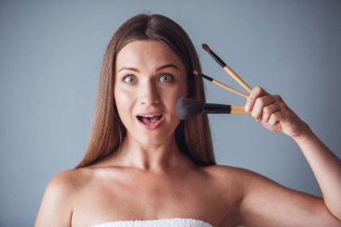 Güzel kadın çıplak omuz ile makyaj fırçaları tutarak ve gri arka plan üzerine açık ağzı ile kameraya bakıyor