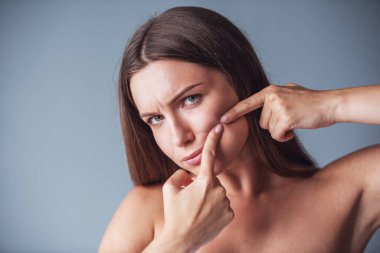 Güzel kadın çıplak omuz ile sivilce sıkma ve gri arka plan üzerinde kamera bakıyor