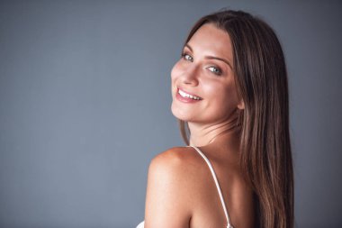 Güzel kadın kameraya bakarak ve gri arka plan üzerinde gülümseyen