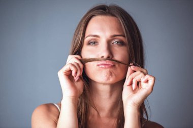 Güzel kadının saçını bıyığını yapma ve gri arka plan üzerinde kamera bakıyor