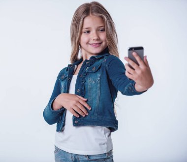 Güzel küçük bir kız bir akıllı telefon kullanarak ve gülümseyen, açık renkli selfie yapıyor