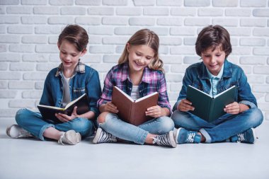 Şirin çocuklara kitap okuma ve yerde otururken gülümseyen
