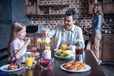 Mutlu bir aile mutfakta kahvaltı. Annem gözleme yaparken baba ve kızı masada oturuyor
