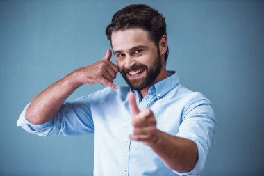 Yakışıklı sakallı iş adamı akıllı rahat kıyafet el telefon, kamera işaret ve gülümseyen, gri arka plan üzerinde gösterilen