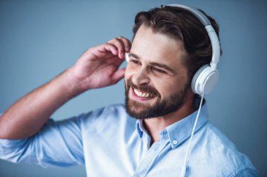 Yakışıklı sakallı işadamı zeki rahat kıyafet ve kulaklık müzik ve gri arka plan üzerinde gülümseyen