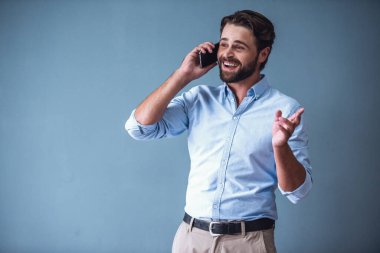 Akıllı rahat kıyafet yakışıklı sakallı işadamı cep telefonda konuşurken ve gri arka plan üzerinde gülümseyen