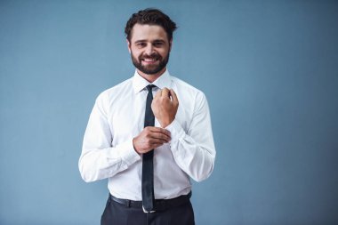 Kameraya bakarak ve gri arka plan üzerinde gülümseyen yakışıklı sakallı işadamı resmi kıyafetli onun kol düğmeleri, uyum sağlıyor.