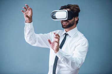 Resmi kıyafetli yakışıklı sakallı işadamı 3d sanal gerçeklik gözlük kullanma ve gri arka plan üzerinde gülümseyen