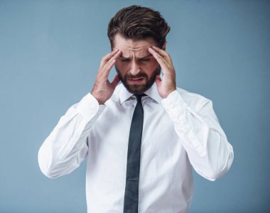 Resmi kıyafetli yakışıklı sakallı işadamı kafasını bir baş ağrısı, gri arka plan üzerinde sahip dokunuyor