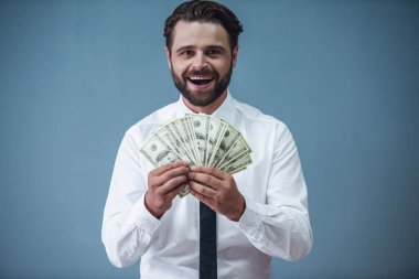 Resmi kıyafetli yakışıklı sakallı işadamı para holding, kameraya bakıyor ve gülümsüyor, gri arka plan üzerinde