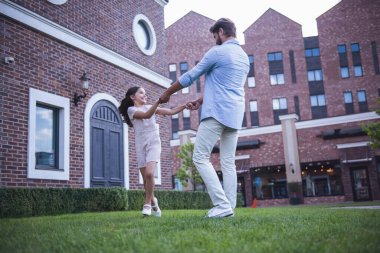 Yakışıklı sakallı baba ve sevimli küçük kızını tutuşup, yuvarlak gidiş yuvarlak ve birlikte dışarıda oynarken gülümseyerek.