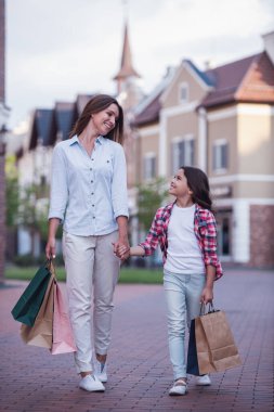 Güzel anne ve sevimli küçük kızını alışveriş çantaları taşırken, el ele tutuşarak ve sokakta yürürken gülümseyen