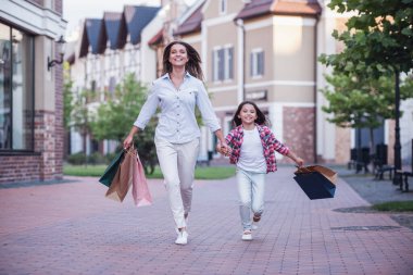 Güzel anne ve sevimli küçük kızını alışveriş çantaları taşırken, el ele tutuşarak ve sokakta yürürken gülümseyen