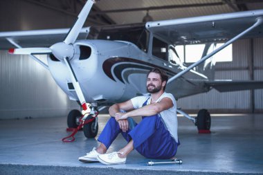 Tek tip uzağa görünümlü ve yakın uçak hangar katında oturan yakışıklı sakallı makinist