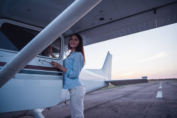 Beautiful woman is looking at camera and smiling while standing outside near the aircraft