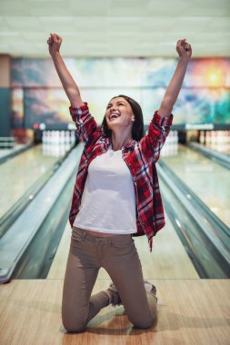 Güzel kız ellerinde yumruk yükselterek ve dizlerinin üzerinde bowling salonu üzerinde ayakta gülümseyen