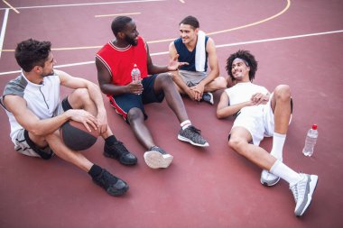 Yakışıklı basketbolcular konuşuyor ve basketbol sahası üzerinde açık havada maçtan sonra otururken gülümseyen