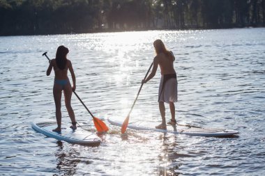 Güzel genç çift Nehri üzerinde sörf Sup, güneş batıyor