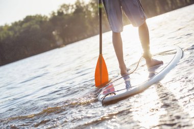 Yakışıklı genç Sup sörf Nehri üzerinde Resim kırpılmış, güneş batıyor