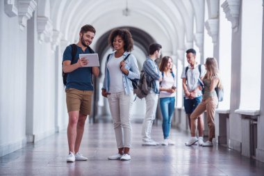 Güzel genç öğrenciler üniversite salonunda dinlenme, bir çift ön planda dijital tablet kullanma ve gülümseyen