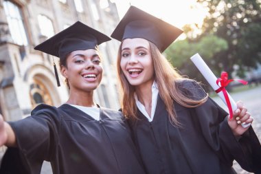 Akademik elbiseler güzel kadın Mezunları Diploma holding, kameraya bakıyor ve açık havada duran süre gülümseyen