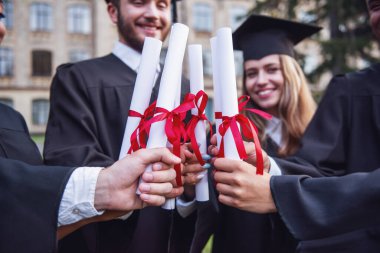 Başarılı mezunlar diploma holding ve açık havada duran süre gülümseyen akademik elbiseler içinde Resim kırpılmış