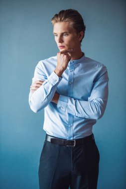 Takım elbiseli yakışıklı dalgın genç işadamı çenesine dokunuyor, uzağa arıyorsunuz ve düşünme, gri arka plan üzerinde