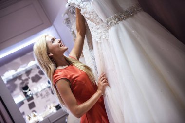 Çekici genç gelin modern düğün salonunun zarif gelinlik seçerken gülümsüyor