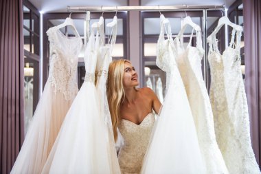 Çekici genç gelin modern düğün salonu gelinlik seçerken gülümsüyor