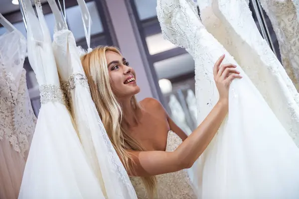 有吸引力的年轻新娘微笑着在现代婚礼沙龙选择婚纱礼服 — 图库照片
