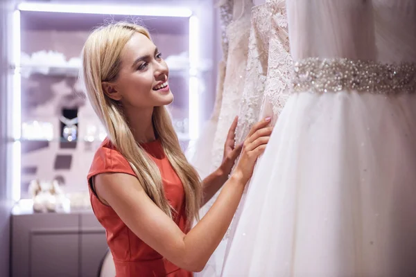 魅力的な若い花嫁は現代のウェディング サロンでエレガントなウェディング ドレスを選択しながら笑っています ストック写真