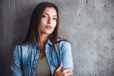 Koyu renk gömlekli çekici bir kadın, arka planda beton duvarda dururken kameraya bakıyor.