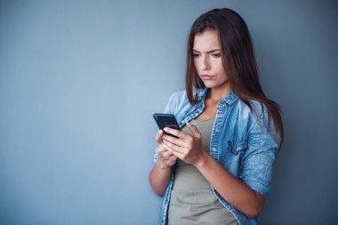 Çekici, koyu renk saçlı kadın gri arka planda akıllı bir telefon kullanıyor.