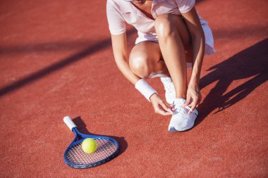 Açık havada tenis oynarken ayakkabılarını bağlayan bir kızın görüntüsü.