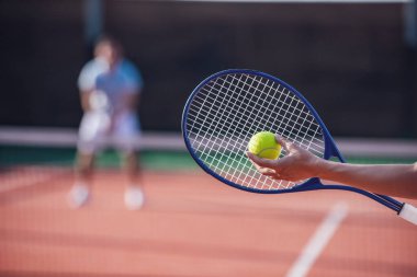Güzel genç bir çift güneşli havada tenis oynuyor, tenis raketi ve top ön planda.