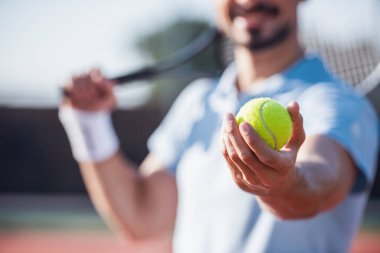 Genç adam açık havada sahada Tenis oynarken Tenis raket ve top tutan kırpılmış görüntü