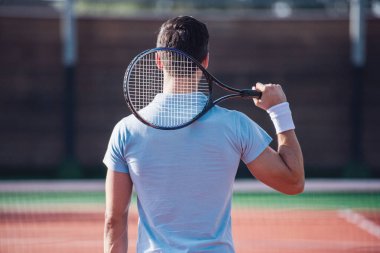 Arkadan görünüşü genç adam açık havada sahada Tenis oynarken tenis raketi holding