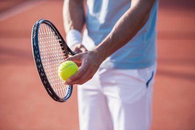 Açık tenis kortunda tenis oynayan yakışıklı bir adamın kırpılmış görüntüsü.