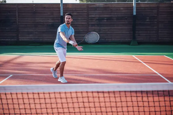 Handsome man is playing tennis on tennis court outdoors